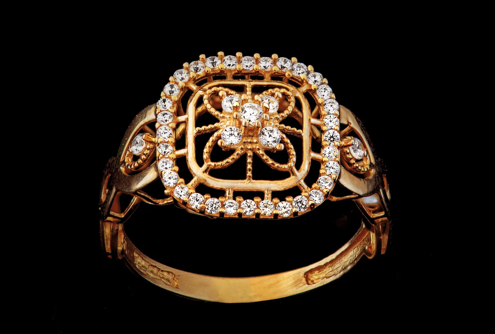 An ornate gold ring with a diamond-set filigree top, on black