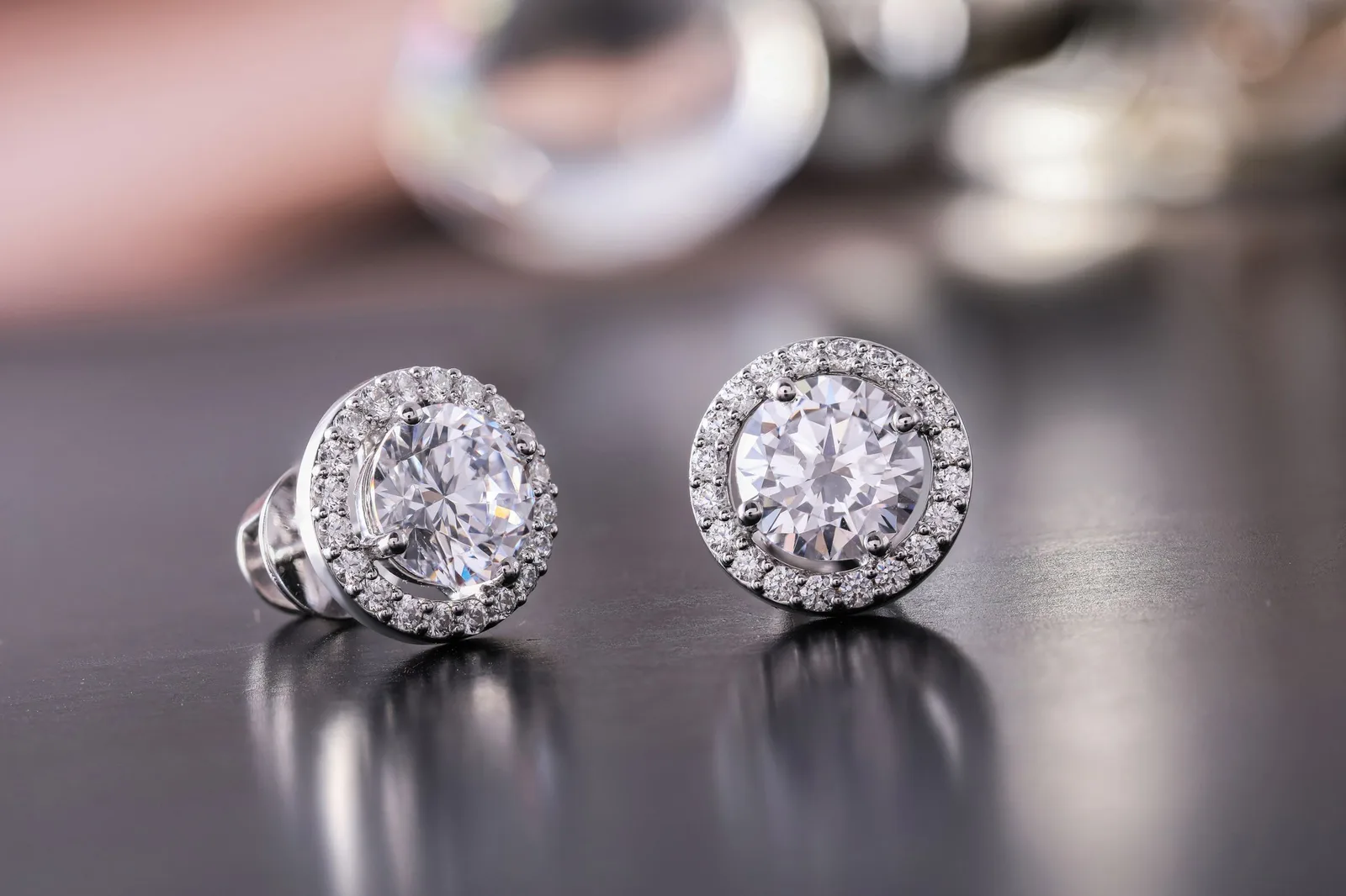 A pair of round diamond halo studs on a dark surface