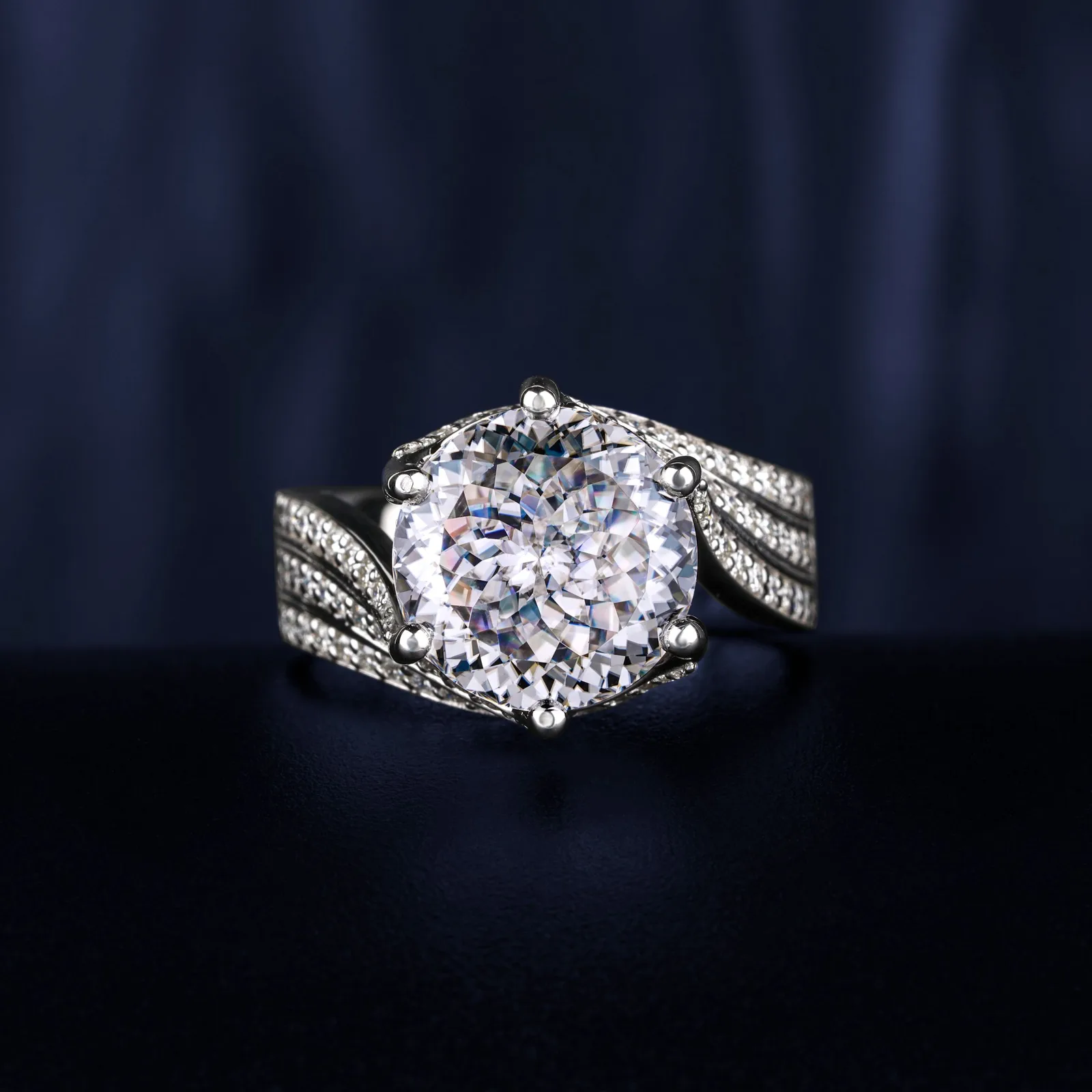A ring with a large round diamond and pavé shoulders, on navy velvet
