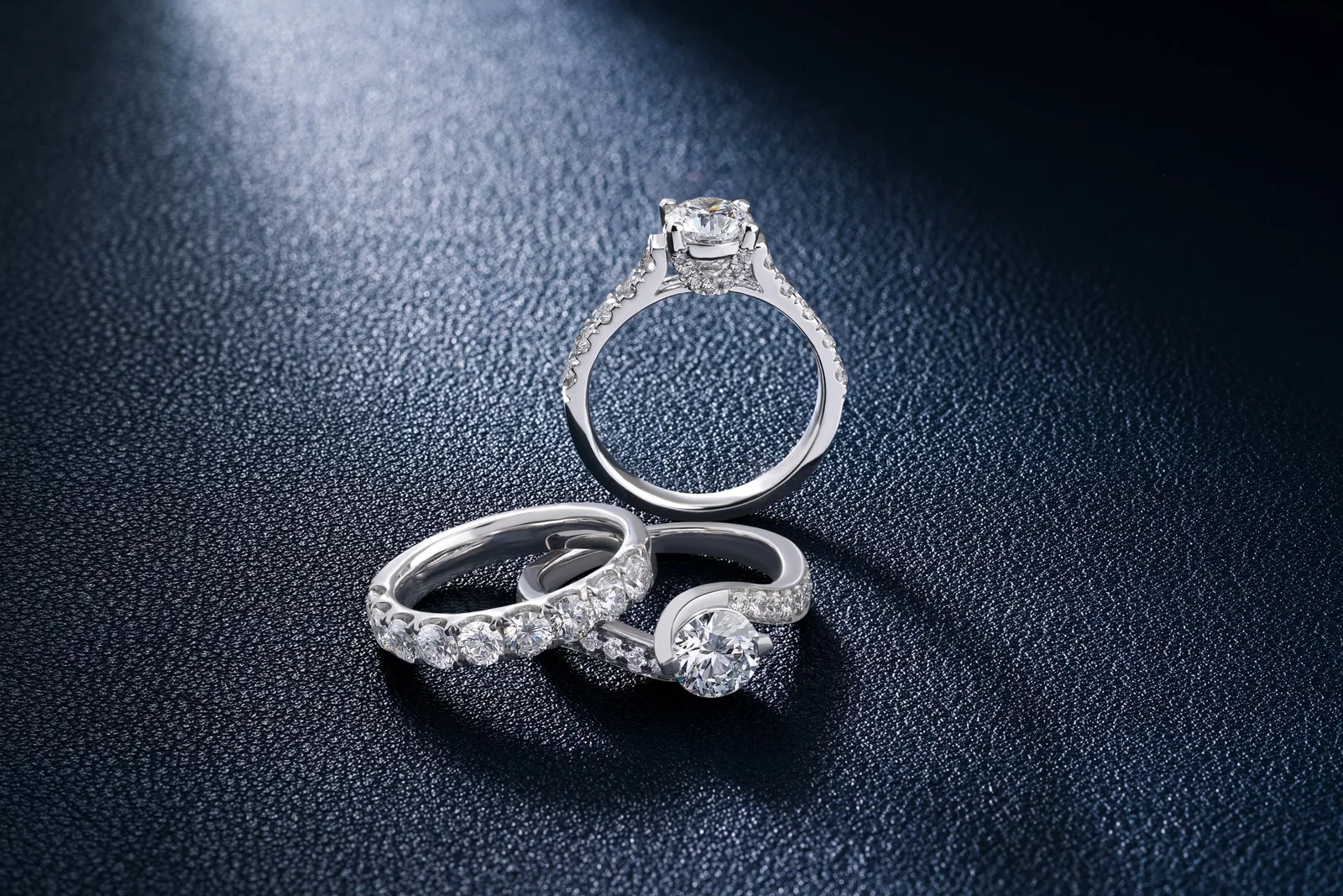 Three diamond rings, one standing, on navy leather
