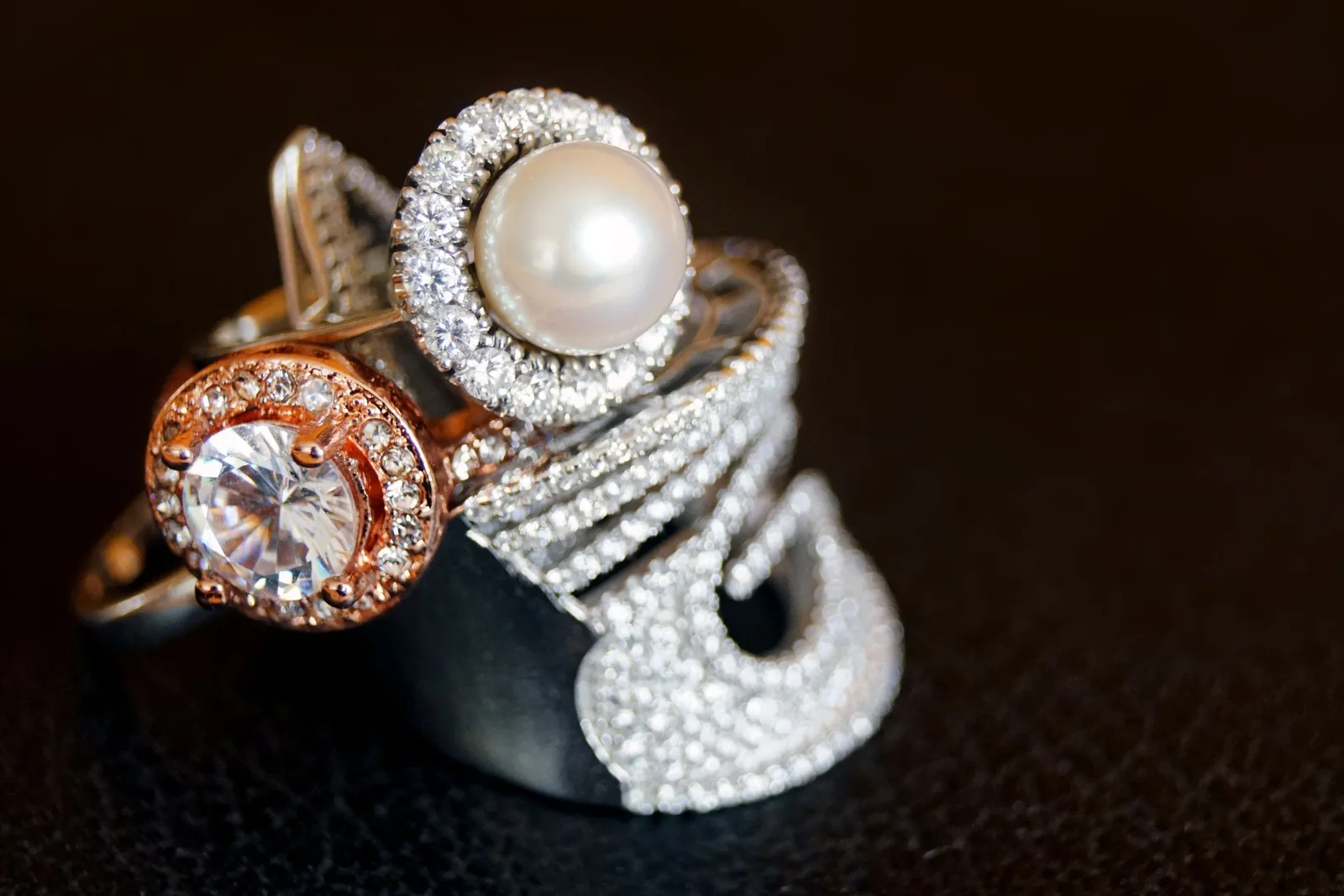 Rose gold, pearl and diamond rings stacked on a dark ground
