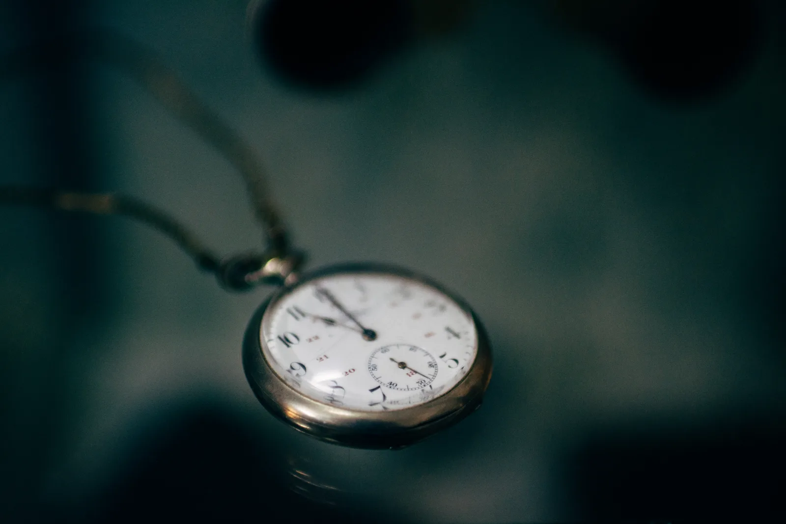 An antique pocket watch on its chain, lying on a dark teal surface
