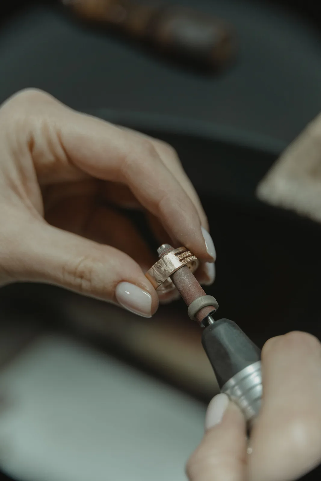 Hands polishing a rose-gold ring with a small rotary tool