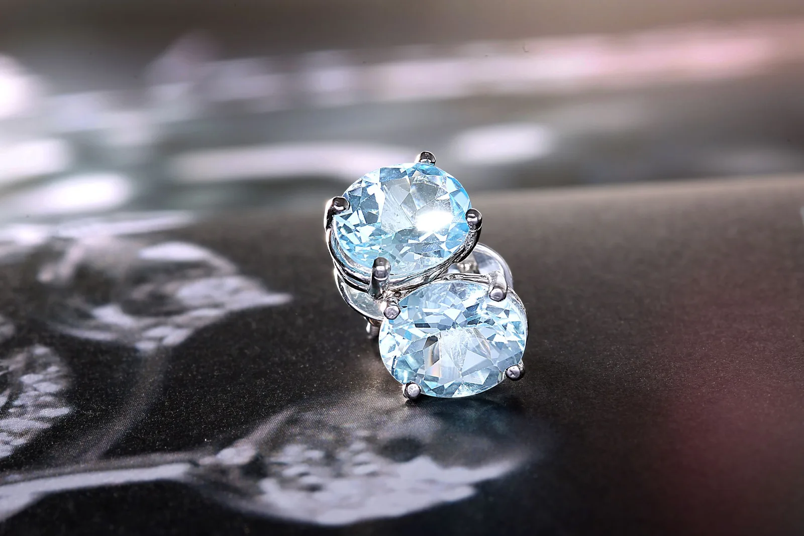 A pair of oval blue stud earrings in white gold, on a dark surface