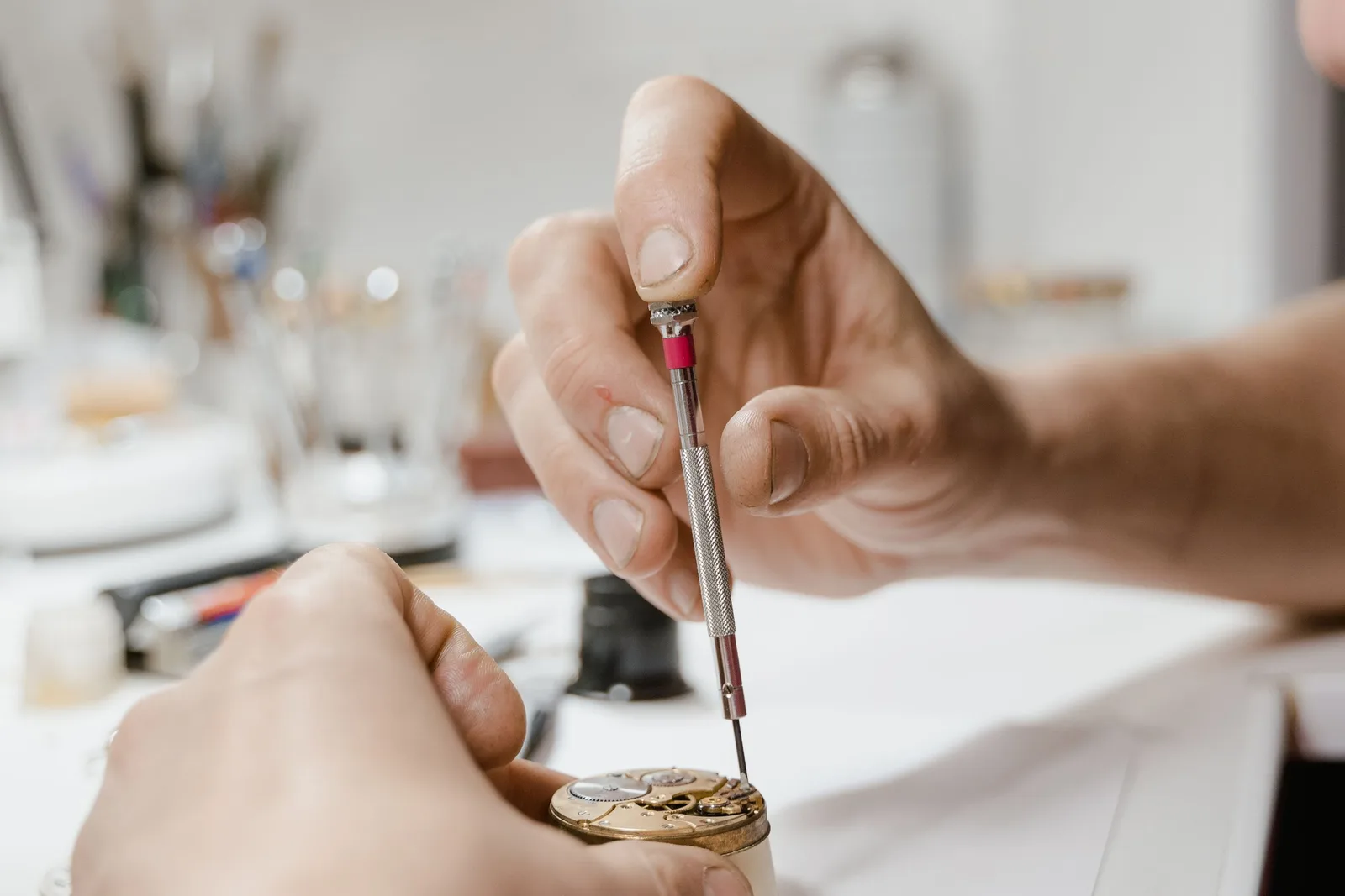 Hands working on an open watch with a fine watchmaker's screwdriver